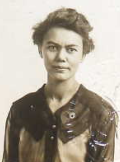 Ursula Tibbels, from her 1920 application for a United States passport; a woman with short dark hair, wearing a dark blouse with a wide round collar