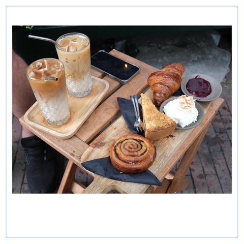 Ein kleiner Tisch auf Backsteinfußweg, gefüllt mit zwei Eiskaffee, Apfelkuchen, Zimtschnecke, Croissant, Schlagsahne und Marmelade.