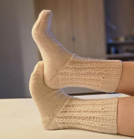 Zwei Füße mit selbst gestrickten, weißen Socken liegen entspannt übereinander. Die Socken zeigen ein feines, strukturiertes Strickmuster aus weicher Wolle.