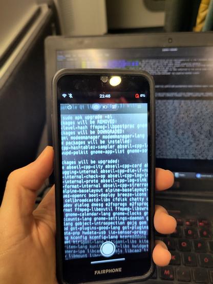 Fairphone 3, camera app preview with the rear camera showing a terminal with some text, captured from the laptop behind the phone.