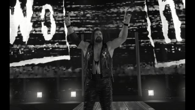 The game scene is a first-person perspective from inside a wrestling ring. In the center, theres a character holding their arms up in victory pose. The background features a large screen with the text WORLD repeated vertically in a distressed font on a brick wall texture. Below the screen are additional details like scoreboards and possibly UI elements for gameplay, but they are too small to discern clearly.