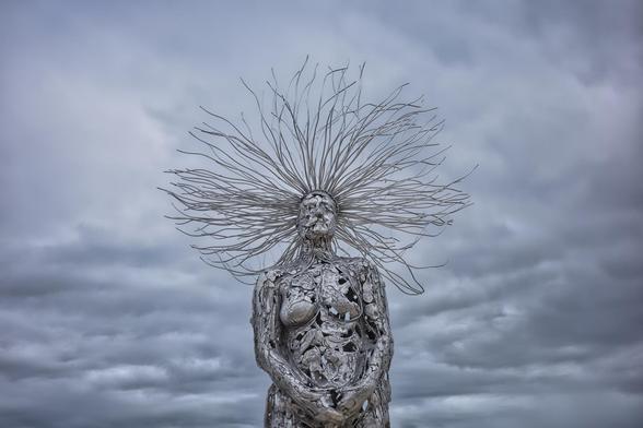 Auto-generated description: A striking metal sculpture depicts a human figure with a complex, branching crown against a cloudy sky.