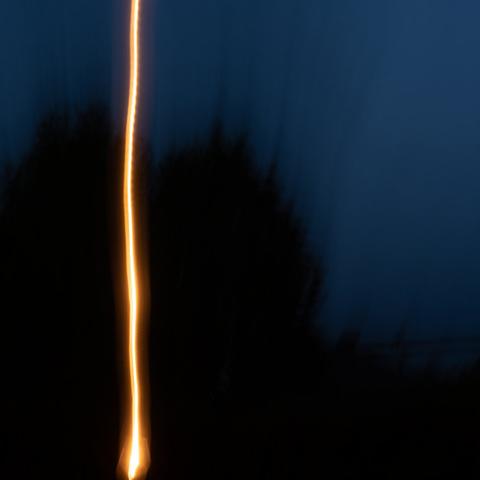 loscil Umbel cover artwork. A blurred photo featuring what seems dark blue sky, dark trees and a light trail of some lantern.