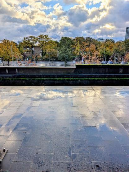 wokiger Himmel spiegelt sich auf einem nassen Bahnsteig