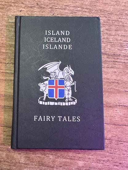 Kämmenen kokoinen pieni musta kirja jonka kannessa on islannin vaakunan ympärillä lehmä, kissa, lohikäärme ja parrakas mies.
Kannessa lukee
ISLAND
ICELAND
ISLANDE
FAIRY TALES