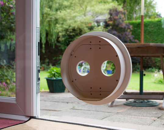 A white Petflap draughtproof pet door set into glass, viewed from indoors