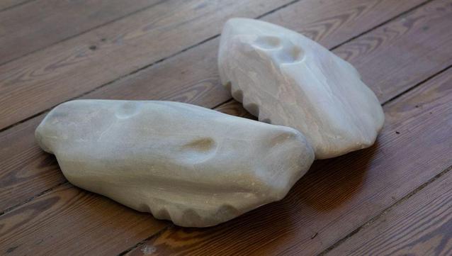 Image: photo of what looks like two pale stones with slight marbling; but they have curving shapes that resemble teeth, and pits that may also be manufactured; they are resting on a wooden surface of laths • “Diagonal Acts is an ambitious new multi-platform project by Marie Farrington spanning 2025. Beginning at the entrance of Kunstverein Aughrim in Spring 2025, the project continues with public workshops at Temple Bar Gallery + Studios, Dublin, and culminates with exhibitions at The Dock, Carrick-on-Shannon and Commonage Projects, London.    ‘Diagonal Acts’ refers to how diagonal lines are seen as ways to connect, divide and move across various places or ideas. The exhibition explores themes of memory, place and connection — exploring gaps, fragments and edges within archaeology, geology, sculpture and staged performance. There is a significant focus on how the human body connects to these themes. The exhibition includes sculptures made from a range of materials, including wax…“