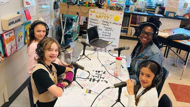 Alameda Post - Love Elementary Fourth and Fifth graders sit at a table in their classroom with podcast equipment. Three students sit with an adult woman, and they all smile at the camera.