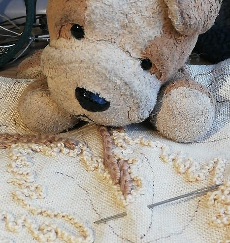 A small fawn plushie dog inspects some hand embroidery in progress.