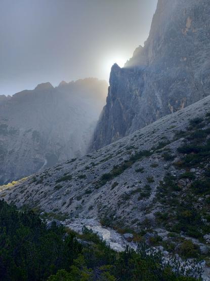 The sun slowly sun emerges from behind the stark outline of the Pale Mountains. A stream of water flows below.
