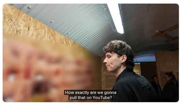 Still of youtuber Daniel Howell standing in front of the vulva diversity wall in the Vagina Museum. An entire wall of photos of vulvas is blurred out. Subtitles read "how exactly are we gonna put that on youtube?"