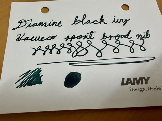 A piece of paper with handwritten text labeled "Diamine black ivy," along with the phrase "Kaweco sport broad nib" and decorative ink swirls. There are also ink swatches: a thick green line and a circular dark green spot.