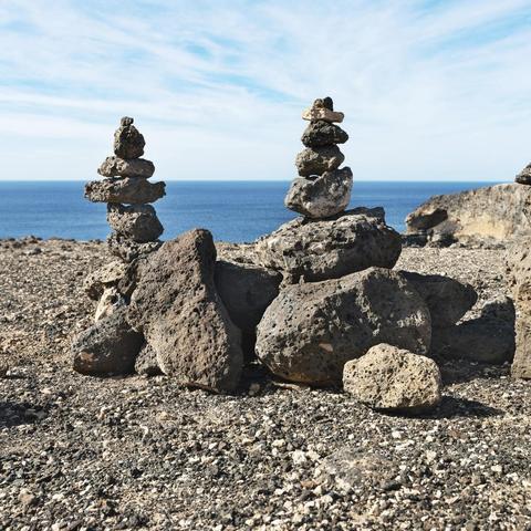 große Felsbrocken mit kleineren aufgeschichteten Steinen, im Hintergrund ist ein Meer zu sehen