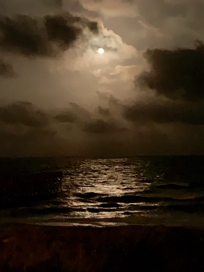 A full moon shines through clouds over a dark, gently rippling ocean.