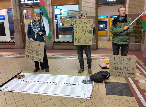 Three protest signs and a banner with a list of names of victims: They have names