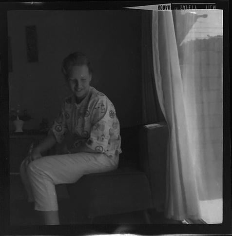 Black and white image of a woman sitting beside a window, looking down at the floor and smiling.