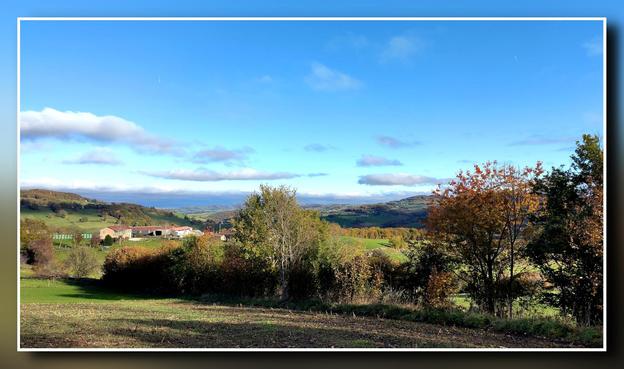 Au premier plan d'un paysage vallonné, des arbres aux couleurs d'automne laissent voir, sur la gauche, un petit village. Plus loin s'étend une plaine bleutée et au loin on peut distinguer une chaîne de montagnes. Quelques nuages s'étirent dans un ciel bleu.