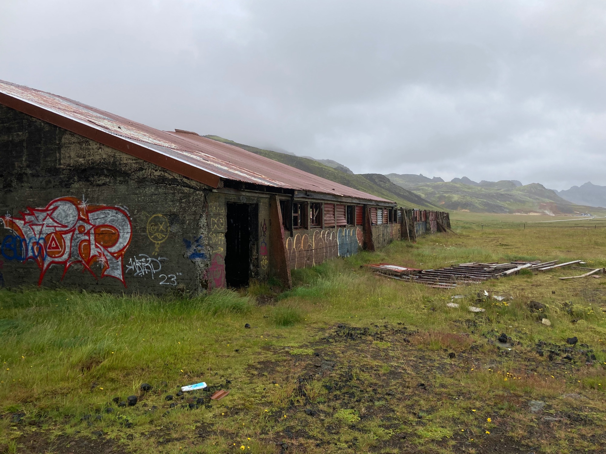 An abandoned old barn covered in graffiti with mountains in the background.