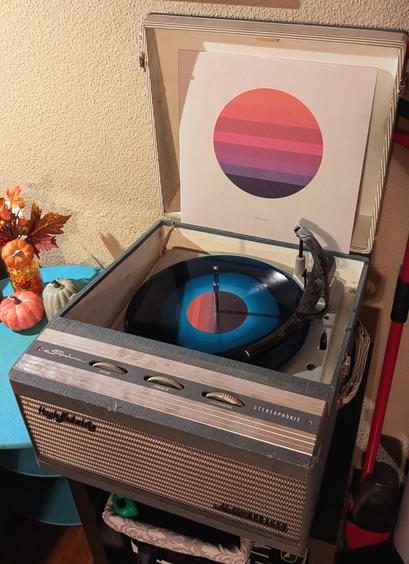 An antique vinyl record player with a vinyl record spinning, playing the album "Awake" by Tycho, with the vinyl cover above it.