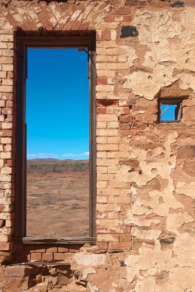 A weathered brick wall with two timber-framed windows (without the glass - long since smashed). One window is big and rectangular. The other small and square.

Through the big window we see Australian outback, some hills, and sky. Through the little window it's just blue sky.