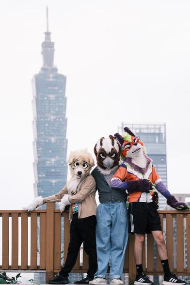 a dog, a gryphon, and a maned wolf fursuiter standing by a railing with Taipei 101 in the background