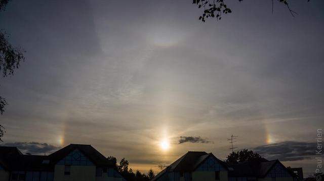 Photo en couleur présentant un halo solaire avec notamment ses 2 parhélies et même, un arc tangent, au-dessus des toits.