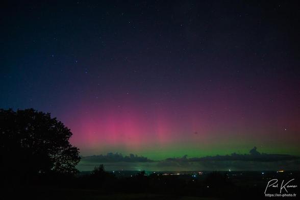 Photographie en couleur, présentant une aurore, boréale, verte près de l'horizon et rose, au-dessus, sous un ciel étoilé.