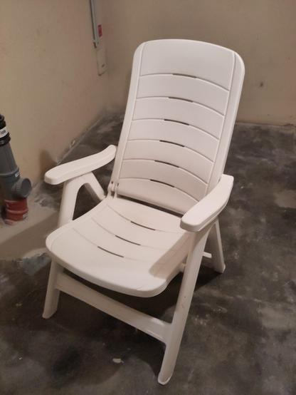 Ein aufgebauter weißer Gartenstuhl aus Kunststoff in einem Kellerraum.