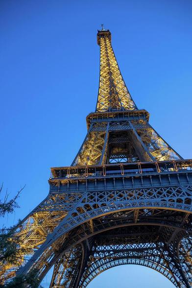 A striking view of the Eiffel Tower illuminated against the twilight sky in Paris, France. The perspective captures the grandeur and iconic status of this world-famous landmark.