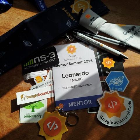 Google Summer of Code Mentor Summit 2025 Leonardo Taccari (The NetBSD Foundation), Mentor badge with several swag and stickers from the event.