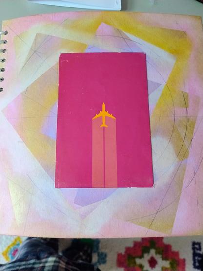 A pink postcard of an aeroplane on a book cover. The cover is mostly brown but there are abstract shapes in purple, pink, and green around it