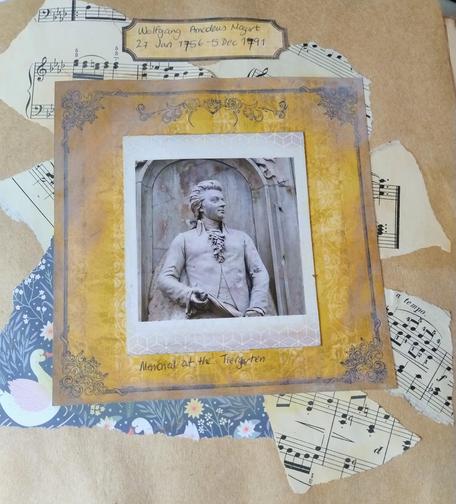 A photo of the statue of Mozart in Berlin tiergarten, from the beethoven-haydn-mozart memorial. It is framed by an aged decorative yellow frame with music sheets in the background