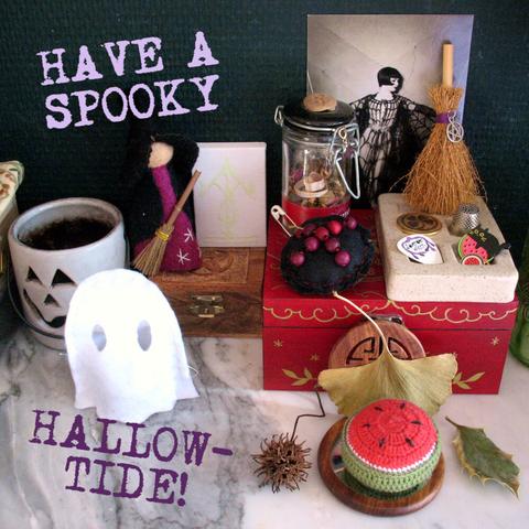 Photo of a part of my Samhain altar on my mantlepiece. It includes a crochet watermelon pincushion surround with symbolically protective plants like a holly leaf. There's also a felt ghost (on top of an electric tea light), a painted red wooden box, a 1920s photo postcard, a felt witch doll, a black protective charm with red beads, and a tiny decorative broomstick.