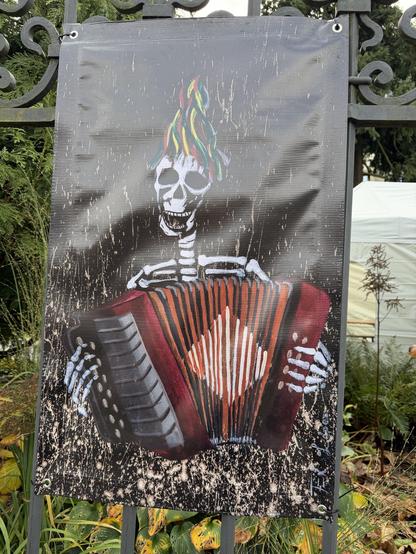 Ein Plakat zeigt ein farbenfrohes Skelett, welches ein Arkodeon spielt
A poster shows a colorful skeleton playing an accordion