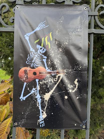 Ein Plakat zeigt ein farbenfrohes Skelett, welches eine Gitarre spielt
A poster shows a colorful skeleton playing a Guitar