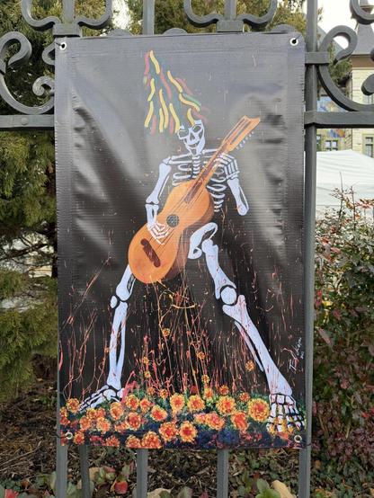 Ein Plakat zeigt ein farbenfrohes Skelett, welches eine Gitarre spielt
A poster shows a colorful skeleton playing a Guitar
