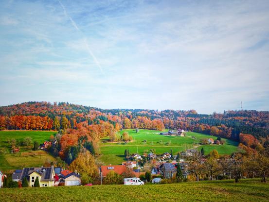 A small village in the Swabian Alps and white clouds above. The trees appear in colourful red, brown, yellow and green.