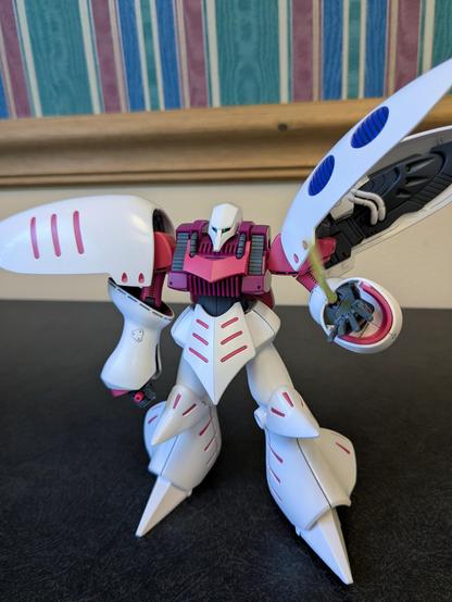 The HG Qubeleu casually standing and shooting a beam out of its left wrist at the viewer