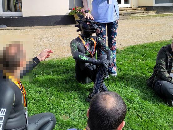 Righin and a couple of other aquafurs folk are sitting on the grass outside the hotel while the sun is out.  Righin's handler is patting his shiny dragon head and his head is at an angle giving the impression he is smiling happily.