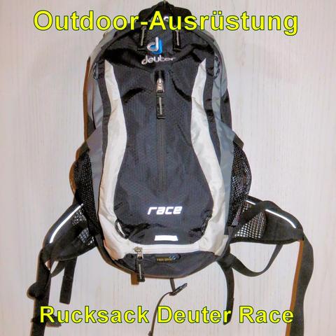 Ein schwarzer Rucksack der Marke Deuter, Modell Race, hängt an einer Wand. Der Rucksack ist schlank und kompakt, ideal für sportliche Aktivitäten wie Radfahren oder Laufen. Er hat weiße reflektierende Streifen an den Seiten und einen zentralen Reißverschluss. Am unteren Teil befindet sich ein Fach mit einem Hinweis auf eine integrierte Regenhülle (Rain Cover). Der Rucksack verfügt über atmungsaktive Schultergurte sowie seitliche Netzfächer für zusätzlichen Stauraum.