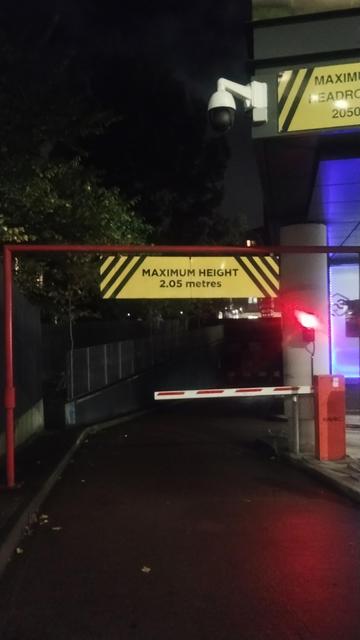 A red and white reflective traffic barrier arm with maximum height warning above it, on the entrance slope to an underground carpark at night