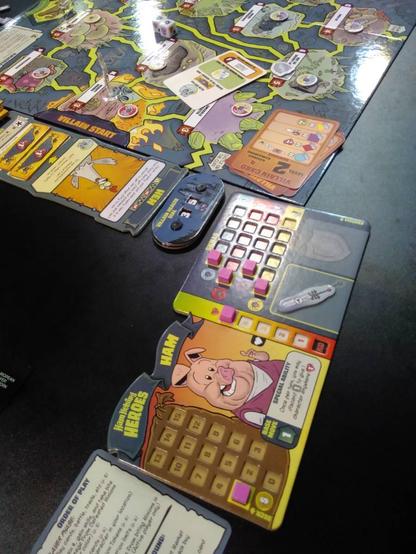 Das Brettspiel „Ham Helsing“, schräg von oben fotografiert. Hinten der Spielplan mit mehreren miteinander verbundenen Wegen und größeren Feldern an deren Kreuzungen. Vorne das Spieltableau von Ham, mit mehreren kleinen rosafarbenen Würfeln als Punktemarker.