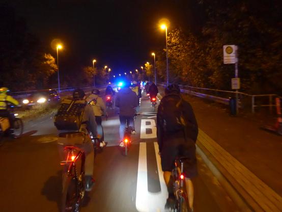 Menschen auf Fahrrädern fahren im Dunkeln auf eine Brücke (Maximilian-Kolbe-Brücke Bonn)