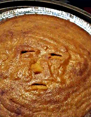 Color photograph.
Someone has poked a knife 3 or 4 times into the surface of a pumpkin pie and it looks like a portrait of Trump.