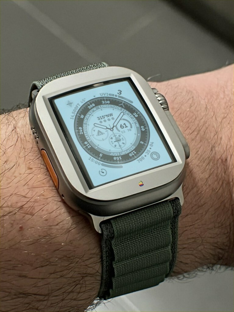 A photo of an Apple Watch Ultra on the wrist of a particularly dashing individual. The display is a greyscale cool-white crt showing a complex watch face theme.