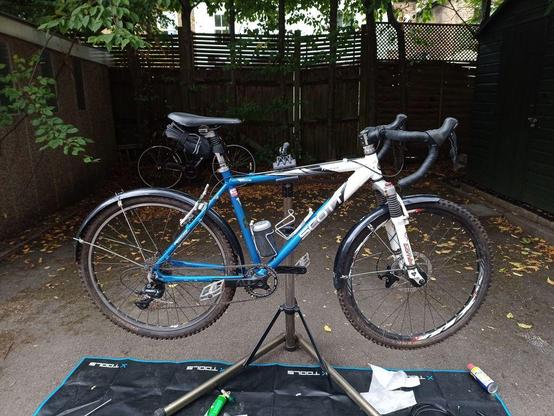 Before: A 2001 Scott Yecora MTB with flat bars & mudguards on a work stand. The frame is blue and white. The Marzocchi Z2 suspension fork is white.