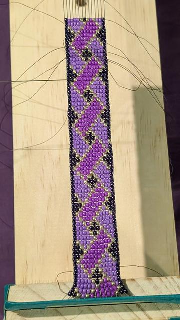 My current beadwork, still on the bead loom. It's a simple geometric pattern in shades of purple and lined with gold.