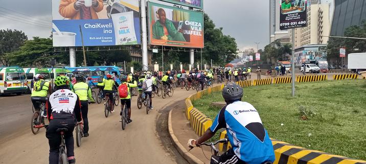 Group of cyclists on a roundabout. Billboards, buses and highrise buildings in the background