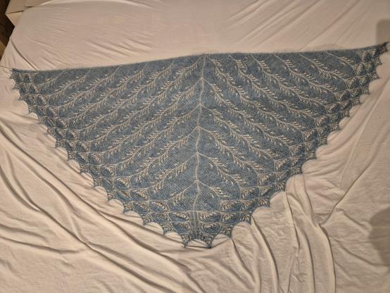 Ein gestricktes Dreieckstuch liegt aufgespannt auf einem weißen Bettlaken