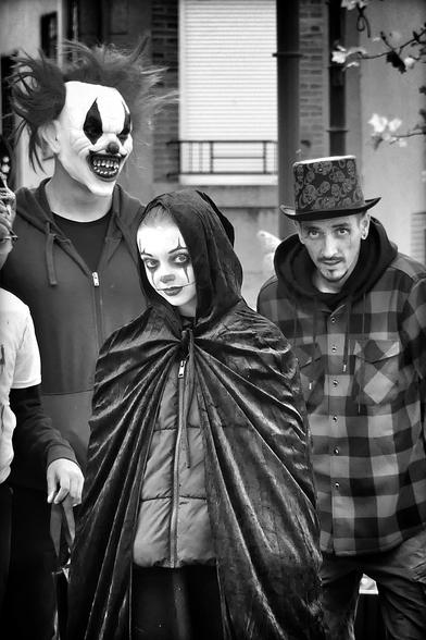 Photo en noir et blanc au format portrait 
Une jeune fille fait la tournée des bonbons avec des amies et des adultes, elle regarde l’objectif .elle est au milieu de la photo, les deux adultes sont derrière, elle est déguisé en clown de ”it”